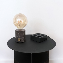 Grijze design stekkerdoos verdeelstekker stekkerblok op zwarte bijzetstafel naast marmeren lamp modern Deens design interieur.